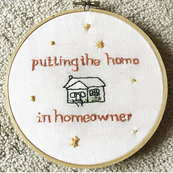 cross stitch in a round wooden frame. Stitching says 'putting the home in homeowner' and has a small stitched house